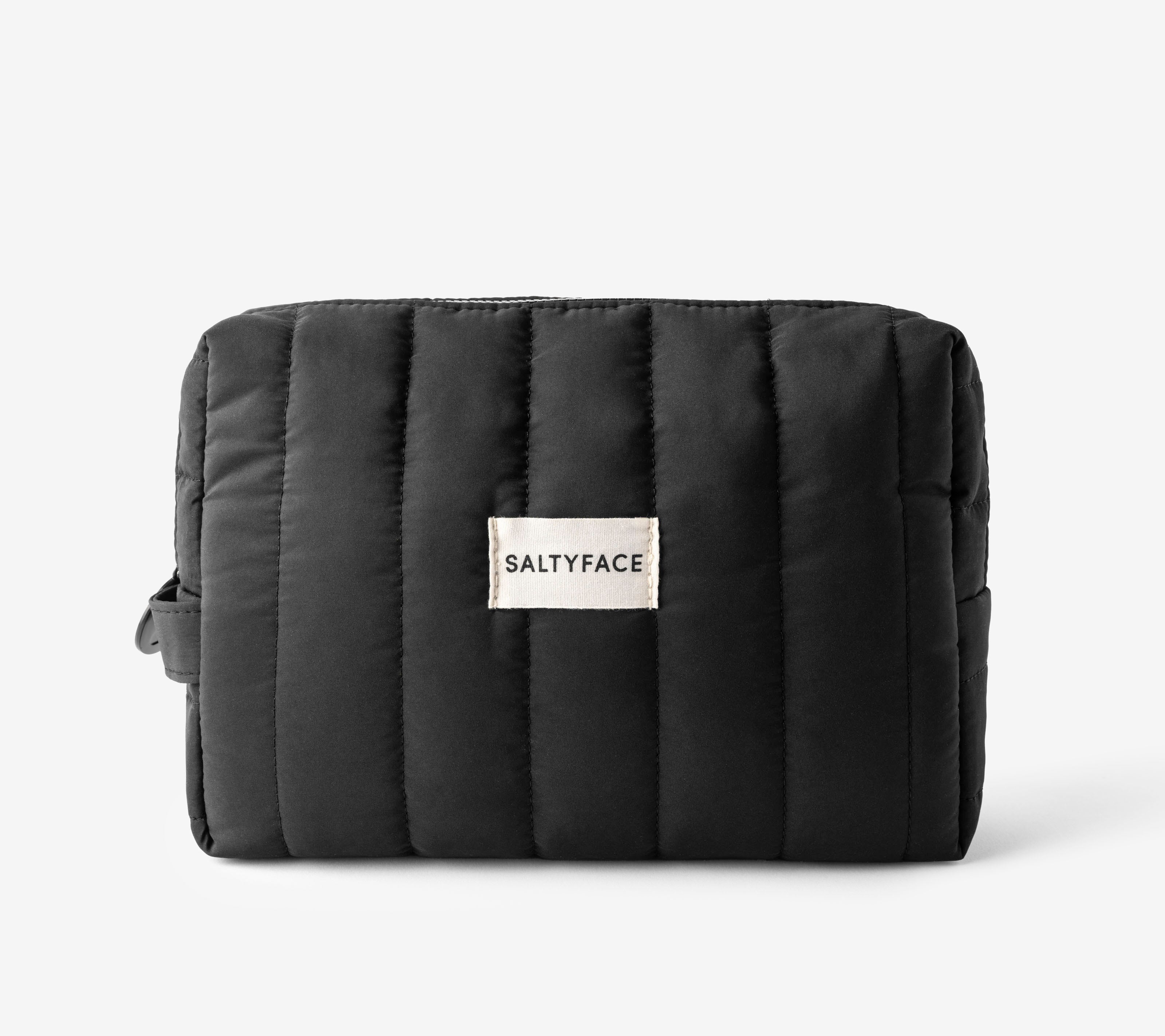 The Everywhere Bag is a black, quilted organizer pouch with vertical stitching and a white SALTYFACE label on the front, shown against a plain white background.