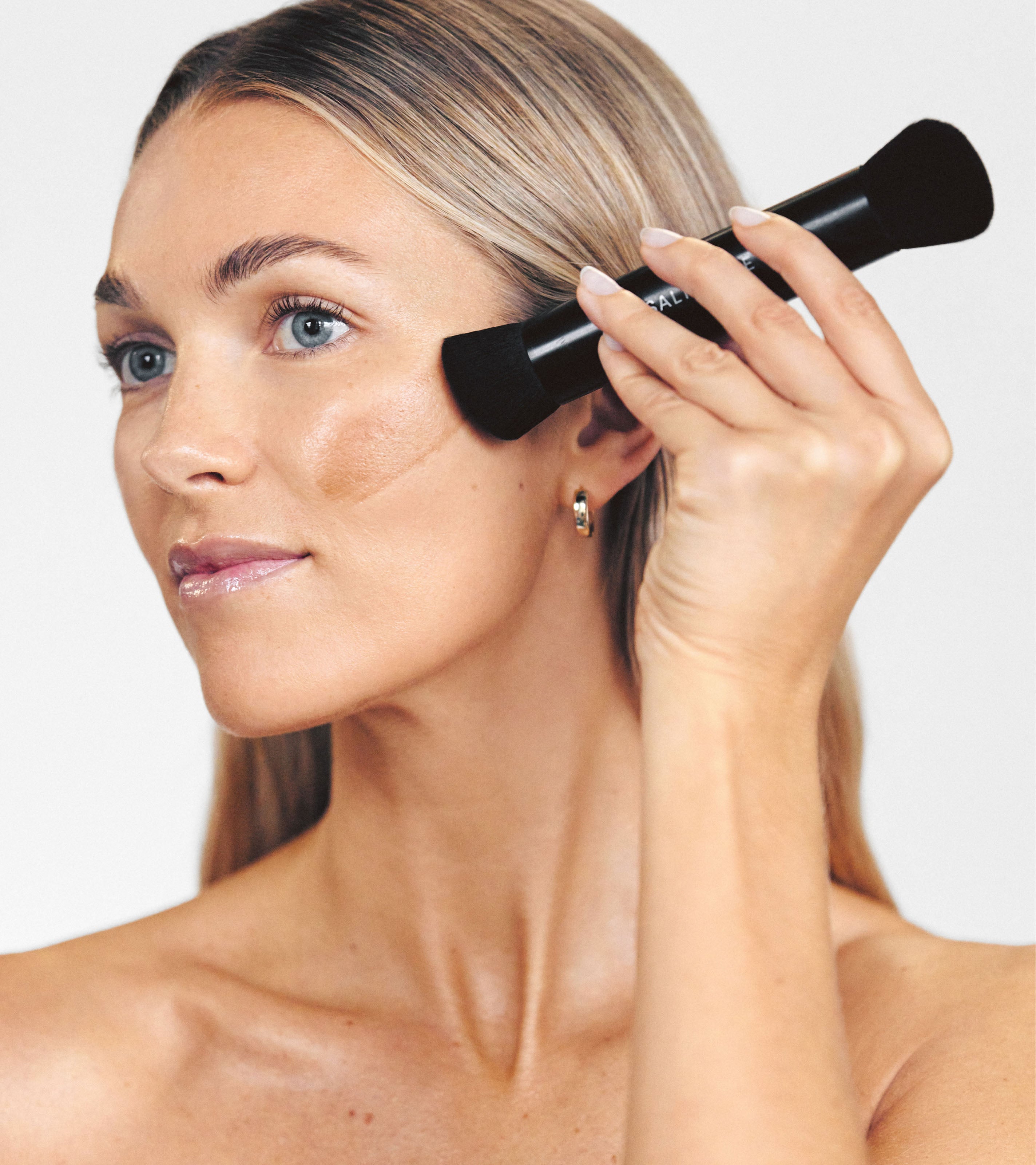 Model applies Liquid Bronzer along the top of her cheekbone with the smaller, angled side of Brush No. 3.