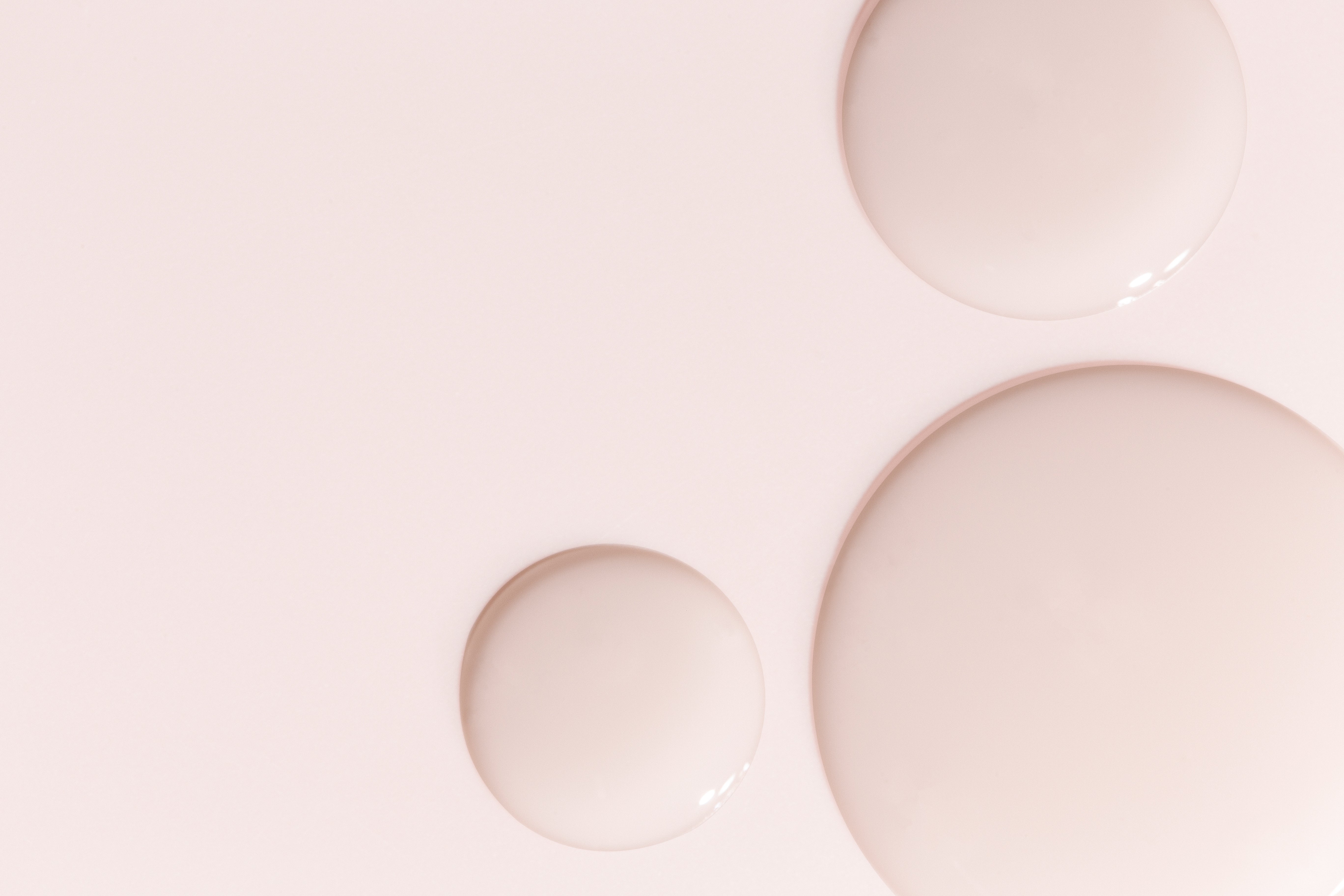 Three glossy, round droplets of varying sizes rest on a smooth pale pink surface, evoking the soothing minimalism of Dr Loretta — Minis in an abstract, soft composition.